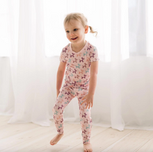 Load image into Gallery viewer, Child wearing pink dog-patterned pajamas standing against a white curtain background