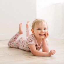 Load image into Gallery viewer, Child in pajamas lying on a light wooden floor with a white background