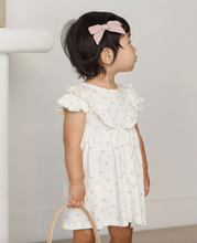 Load image into Gallery viewer, Young child wearing a white dress with ruffled sleeves and holding a small bag.