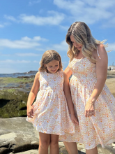 Load image into Gallery viewer, Two women in matching floral dresses standing on a rocky beach with ocean view.