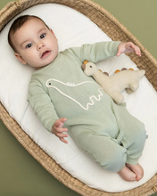 Load image into Gallery viewer, Baby in a green onesie with a dinosaur design, lying on a white cushion in a wicker crib.