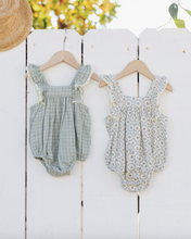 Load image into Gallery viewer, Two baby rompers hanging on a white wooden fence with blurred greenery in the background.
