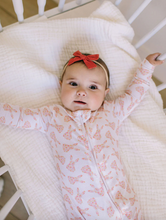 Load image into Gallery viewer, Baby in a crib wearing a pink outfit with bunny patterns and a red bow headband.