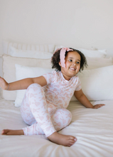 Load image into Gallery viewer, Child in a pink outfit sitting on a white couch