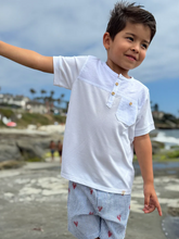 Load image into Gallery viewer, Child wearing a white shirt with a pocket and blue pants with red patterns, standing on a beach.