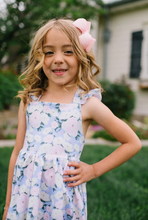 Load image into Gallery viewer, Young girl in a floral dress with a pink bow in her hair, standing outdoors.