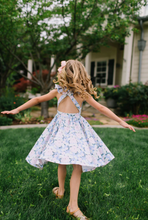 Load image into Gallery viewer, Young girl in a floral dress twirling outdoors on a sunny day.