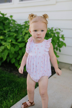 Load image into Gallery viewer, Young child wearing a pink romper with ruffled sleeves outdoors.