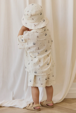 Load image into Gallery viewer, Child wearing a white outfit with black patterns and a matching hat, standing against a white curtain.