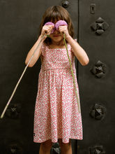 Load image into Gallery viewer, Child in a red floral dress holding a long stick with pink flowers against a dark textured background