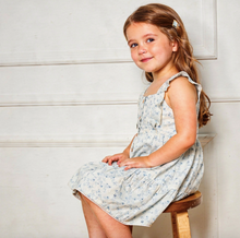Load image into Gallery viewer, Young girl in a floral dress sitting on a wooden stool against a white wall.