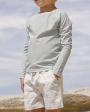 Load image into Gallery viewer, Child wearing a light gray long-sleeve shirt and white shorts with a pattern, standing against a cloudy sky.
