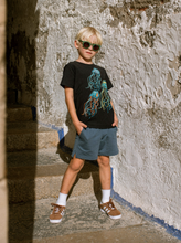 Load image into Gallery viewer, Young boy wearing sunglasses and a black t-shirt with a graphic design, standing against a textured wall.