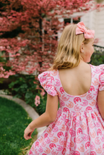 Load image into Gallery viewer, Young girl in a pink dress with horseshoe pattern standing in front of cherry blossoms.