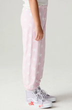 Load image into Gallery viewer, A child wearing light pink jogger pants with a white star pattern, paired with white sneakers, shown from the waist down against a light gray studio background.