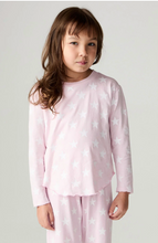Load image into Gallery viewer, A young girl with brown hair wearing a light pink long-sleeve pajama top and matching pants, both printed with a white star pattern, standing against a light gray studio background.
