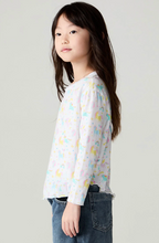 Load image into Gallery viewer, A young girl with long dark hair is shown in profile wearing a white long-sleeve top with a pastel unicorn print and blue jeans, photographed against a plain light gray studio background.