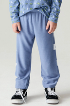 Load image into Gallery viewer, A child wearing dusty blue sweatpants with white graphic accents, a blue patterned long-sleeve shirt, and black low-top sneakers, shown from the waist down against a light gray studio background.