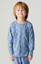 Load image into Gallery viewer, A young boy with light brown hair wearing a light blue long-sleeve shirt with a repeating pattern of green dinosaurs and white lightning bolts, paired with matching light blue pants, standing against a neutral light gray background.