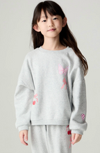 Load image into Gallery viewer, A young girl with long dark hair stands against a light gray studio background wearing a light gray heather sweatshirt and matching sweatpants. The sweatshirt has pink butterfly and cherry graphics, and the pants have small cherry graphics near the lower leg.