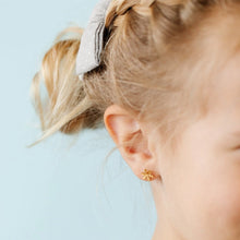 Load image into Gallery viewer, Close-up of a child wearing a gold-tone snowflake stud earring against a pale blue background.