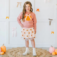 Load image into Gallery viewer, A young girl stands in a decorated indoor setting wearing a pink long-sleeve sweatshirt with a pumpkin-and-bow graphic on the front, a light pink tulle skirt with orange pumpkin prints, and white ankle boots. Pumpkins, a woven rug, and bow decorations are visible around her.