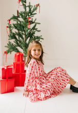 Load image into Gallery viewer, Child seated beside red wrapped gifts in a long-sleeve Dainty Bows dress with the ruffled skirt spread around them.