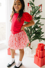 Load image into Gallery viewer, Front view of a child in a pink Dainty Bows tulle skirt and red puff-sleeve top, standing with one hand on their hip.