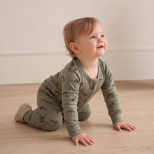 Load image into Gallery viewer, A baby crawling on a light wood floor wearing an olive green long-sleeve sleep suit with a dinosaur print, set against a neutral cream wall background.