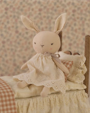 Load image into Gallery viewer, Rylee the Rabbit seated on a miniature bed with cream lace bedding and gingham pillows, wearing an eyelet dress with a neck bow.