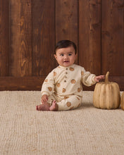 Load image into Gallery viewer, A baby sitting on a textured cream rug in front of a dark wood plank wall, wearing a cream long-sleeve bodysuit with brown acorn prints. A small decorative pumpkin sits to the baby's right.