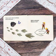 Load image into Gallery viewer, Open book with dinosaur-themed illustrations on a wooden surface