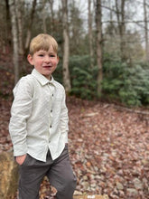 Load image into Gallery viewer, Young boy standing outdoors in a natural setting with trees and fallen leaves.
