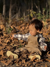 Load image into Gallery viewer, A toddler sitting on a bed of dry autumn leaves outdoors, wearing a gray and white plaid flannel shirt, tan corduroy overalls, and cream-colored shoes.
