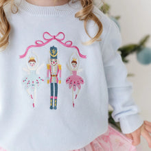 Load image into Gallery viewer, A close-up of a child wearing a white knit sweater with a colorful embroidered design of three ballerina characters under a pink bow, with a softly blurred indoor background.
