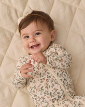 Load image into Gallery viewer, Close-up of a smiling baby wearing a cream Holiday Floral zip footie and bow headband on a quilted blanket.
