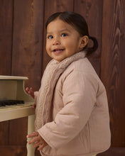 Load image into Gallery viewer, Toddler beside a toy piano wearing the jacket’s smooth pink side outward, with shearling visible along the open front and collar.
