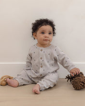 Load image into Gallery viewer, A baby with curly dark hair sits on a light wooden floor against a cream wall, wearing a light gray waffle-knit long-sleeve romper with small dark star prints and a button-up front. The baby is holding a pinecone next to a wooden teething toy.
