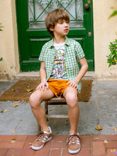 Load image into Gallery viewer, Child sitting on a step wearing a green checkered shirt, orange shorts, and brown shoes in front of a green door.
