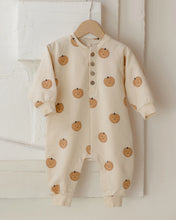 Load image into Gallery viewer, A baby long-sleeve romper in cream with a pumpkin print, hanging on a wooden hanger against a white brick wall.
