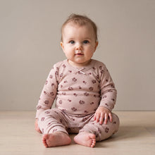 Load image into Gallery viewer, A baby sitting on a light wood floor against a neutral beige wall, wearing a dusty pink long-sleeve footed sleeper with a small brown floral pattern.
