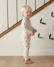 Load image into Gallery viewer, A toddler stands barefoot indoors near a staircase, wearing a cream long-sleeve pajama set with a small repeating boat-and-anchor print. The room has light wood flooring and black bat wall decorations.
