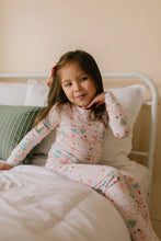Load image into Gallery viewer, Child resting a hand beneath their chin while sitting on a bed in pale pink Sugar Plum pajamas.

