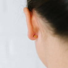 Load image into Gallery viewer, Rear view of an earlobe showing the round gold-tone flat back of a bow stud earring.
