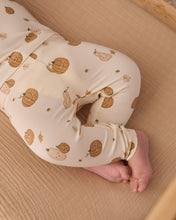Load image into Gallery viewer, A close-up of a baby wearing cream-colored leggings with a brown pumpkin and leaf pattern, lying on a wooden changing surface.
