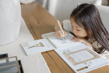 Load image into Gallery viewer, Child leaning over the open Pooh’s Birthday Surprise book, painting an activity page with the water pen.
