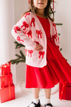 Load image into Gallery viewer, Close-up of the blush pink bow cardigan, showing its open front, red bow motifs, and ribbed cuffs and hem.
