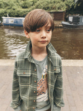 Load image into Gallery viewer, A young boy with brown hair stands outdoors by a canal wearing a green and yellow plaid button-up shirt over a gray t-shirt with a bird graphic.

