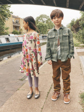 Load image into Gallery viewer, A boy and a girl standing on a canal-side walkway. The girl wears a long-sleeve floral tunic dress over lavender leggings and silver shoes.
