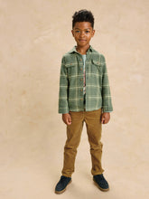 Load image into Gallery viewer, A young boy modeling a green and white plaid button-up shirt over a light blue t-shirt, paired with brown corduroy pants and navy blue sneakers, standing against a textured beige backdrop.
